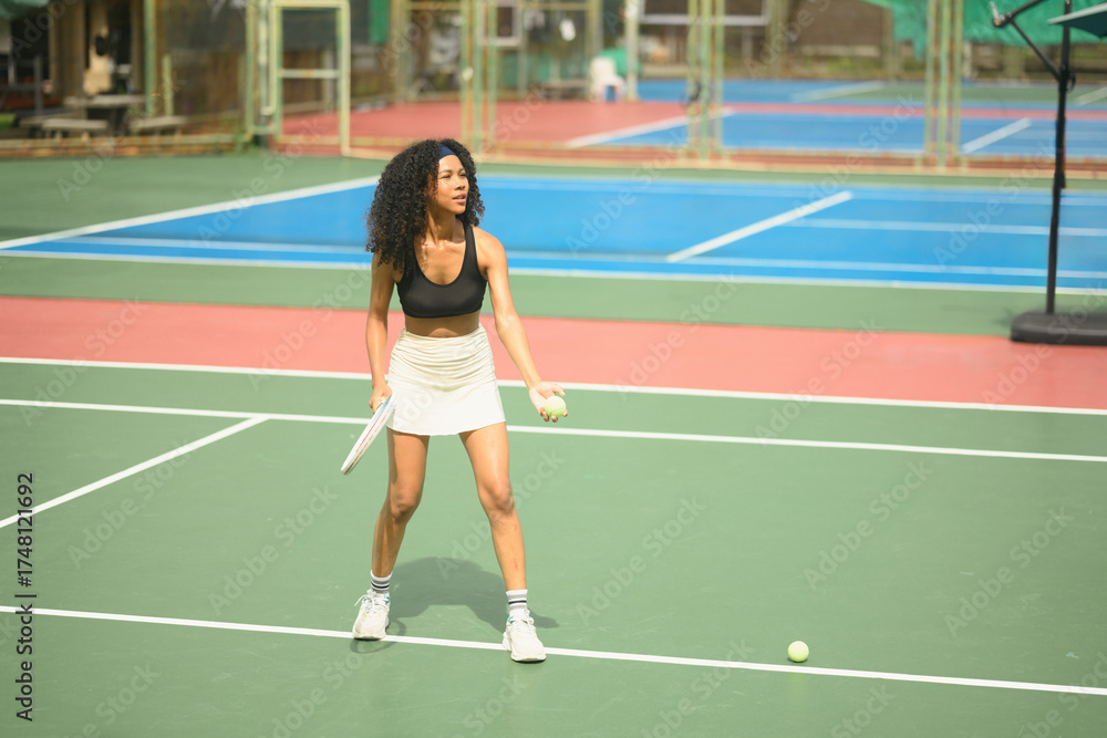 Fototapeta premium African female tennis player preparing to serve the ball on an outdoor court, showing focus, confidence, and athletic strength