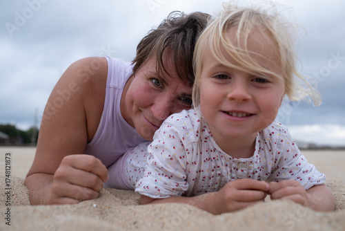 Woman in sportswear relaxing on the beach with her daughter on the sand. 