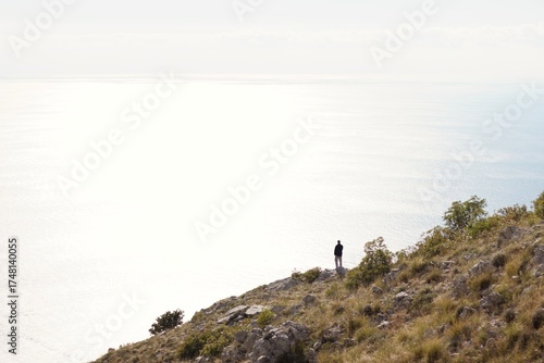 a lonely figure on the mountainside looking at the nothingness behind the mountain