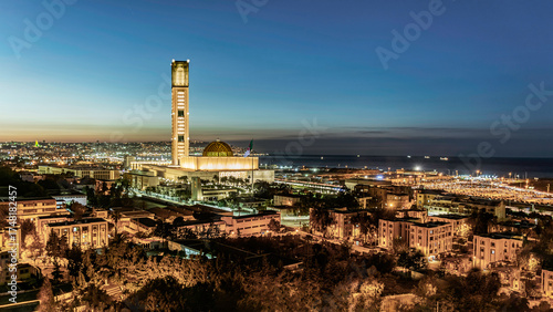The great mosque of Algeria and the Martyr's Memorial at sunset. Buildings, and palm trees, the Marina mall parking and the coastal city bay Mediterranean sea ships enlightened under a colorful sky.