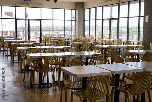 A spacious cafeteria filled with neat rows of white tables and yellow plastic chairs