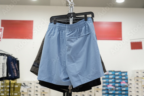 Rear view of light blue athletic shorts with a zippered pocket hanging on a display rack in a clothing store with shoe boxes in the background