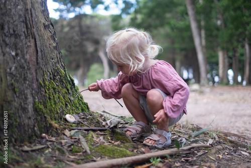 Blonde girl found a mushroom in the forest and pokes it with a stick