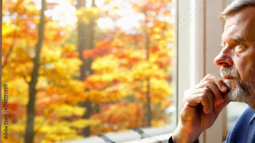 Man contemplating by window, autumn leaves visible. Possible office setting