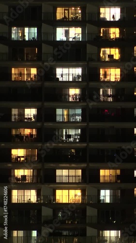 TOKYO, JAPAN - AUG 2025 : Time lapse shot of illuminated modern high rise residential apartment building with glowing windows in dense urban cityscape at night. Lifestyle and real estate concept.