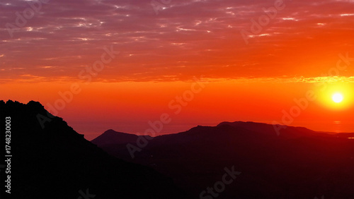 Aerial view of the sun setting over the dark silhouette of Table Mountain and the Cape Peninsula, the sky ablaze with fiery hues, Cape Town, Western Cape, South Africa.