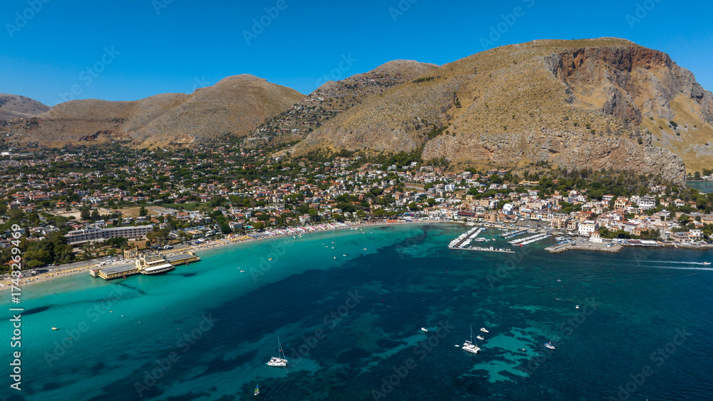 Naklejka premium Aerial view of Mondello beach, located near Palermo, Sicily, Italy. On the left is the Charleston, an Art Nouveau beach club, and on the right is the town's harbor. Many people are on summer vacation.