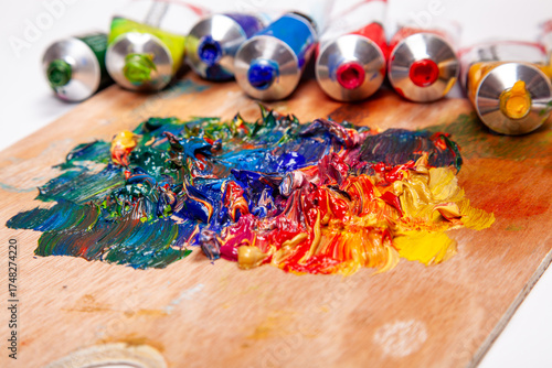 Vibrant oil paints mixed on a wooden artist's palette with tubes of color in the background. A colorful and messy close-up representing the creative process, inspiration, and the joy of painting.