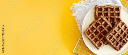 Homemade oat waffles on a white plate on a sunny yellow background copy space