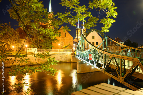 Night scene of the illuminated Tumski Bridge (Most) and Cathedral Island (Ostrów Tumski) in Wroclaw. Poland. Street lights and reflections in the Odra River create a romantic and peaceful atmosphere.