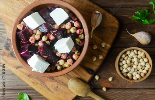 Beet Salad with chickpeas, feta and green sauce with oil and parsley in a ceramic bowl on a wooden table. Rustic style. Healthy eating. Horizontal orientation. Selective focus. Top view.