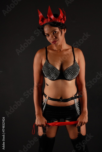 Low key portrait of pretty young dark haired woman in leather lingerie with whip in her hands