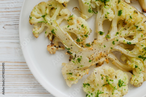 Cauliflower with chimichurri sauce on a white plate on a white wooden background. Concept of vegan and vegetarian food. Healthy eating. Horizontal orientation. Selective focus. Top view. Close up