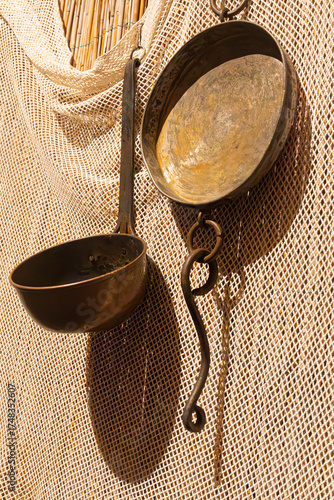 Old-fashioned metal cooking tools displayed against a natural background of netting and bamboo. The image evokes a simple, rustic, and authentic lifestyle.