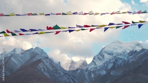 Slow motion shot of Buddhist prayer flags waving in the wind in front of snowy Himalayan mountain peaks with clouds above them as seen from Padum town in Zanskar Valley, Ladakh, India. Scenic view.