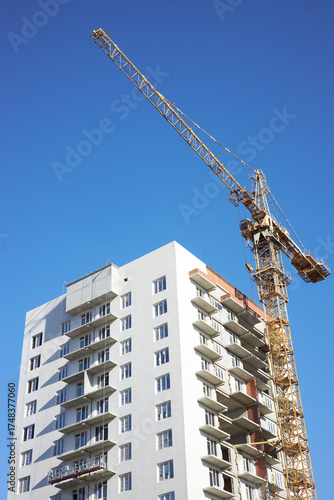 construction crane is positioned beside a tall building under construction. Workers can be seen on the site, preparing for the next stages of the project on a sunny day