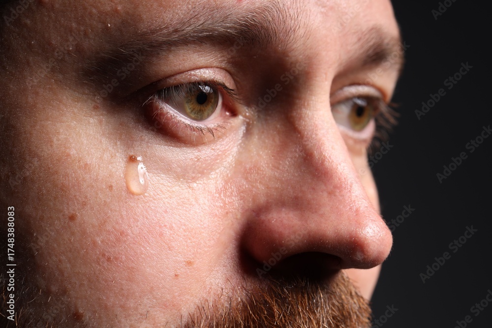 Fototapeta premium Sad man crying on black background, closeup