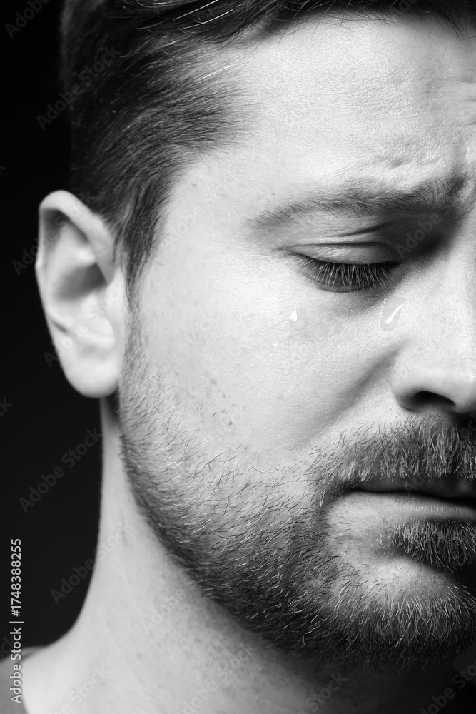 Obraz premium Sad man crying on dark background, closeup. Black and white effect