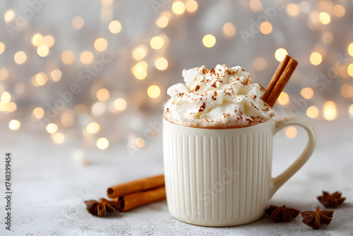 warm mug of cocoa topped with a swirl of whipped cream and a dusting of cinnamon, alongside cinnamon sticks and star anise. A warming winter drink.