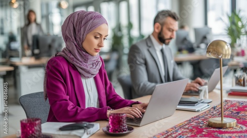 Muslim businesswoman concentrating on her work on a laptop in a diverse and modern office environment
