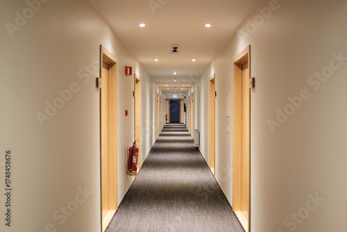 Emptry hotel corridor with carpet floor, wooden doors, fire extinguisher and emergency exit sign