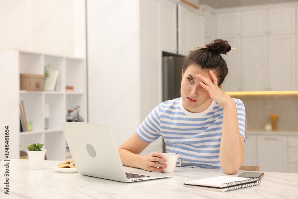 Fototapeta premium Tired woman with cup and laptop at white marble desk in home office. Space for text