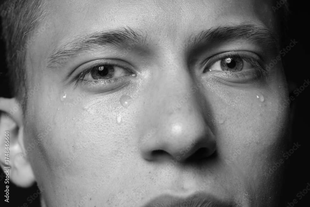 Fototapeta premium Sad man crying on dark background, closeup. Black and white effect