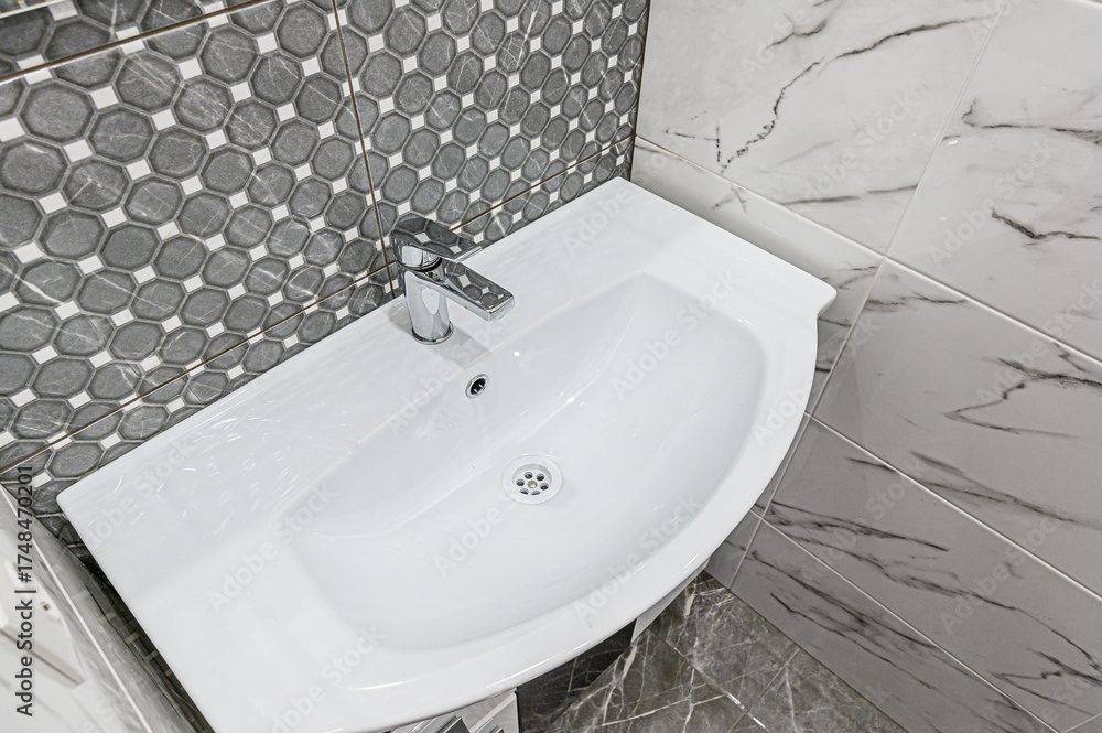 Fototapeta premium crisp, clean bathroom sink with chrome faucet is surrounded by grey-toned tiles. The patterned walls add texture