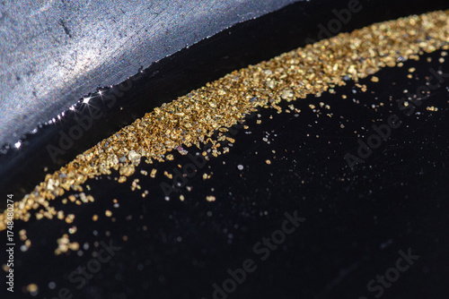 Closeup view of gold flakes collected in a black panning pan. Shiny metallic particles representing mining, prospecting, natural resources, and the search for wealth and treasure.