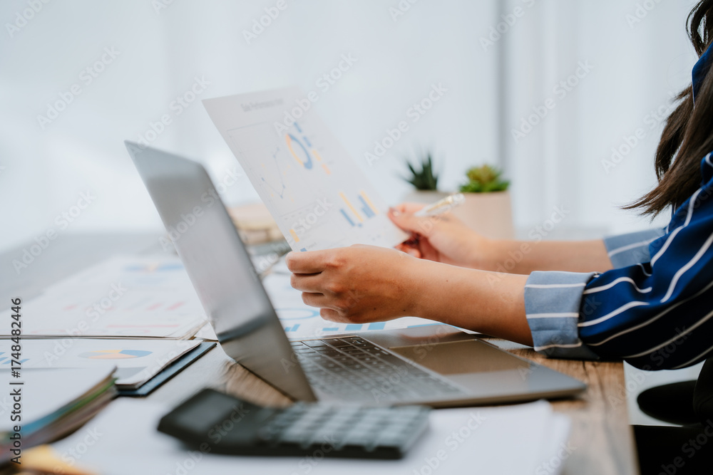Fototapeta premium A beautiful Asian businesswoman analyzes charts using a laptop calculator at the office.