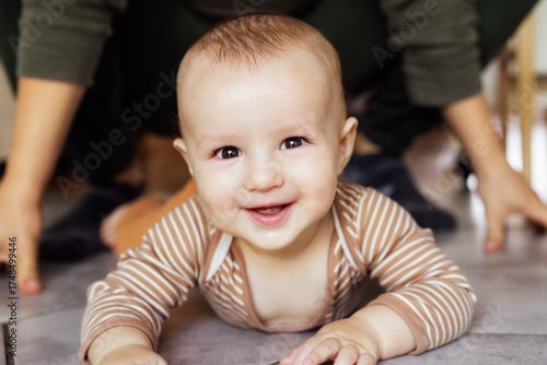 Happy, laughing baby lying on tiled floor at home with no face father on background. Dad And Toddler Child Enjoying Spending Time Together, Cheerful active infant smiling, learning to crawl, playing