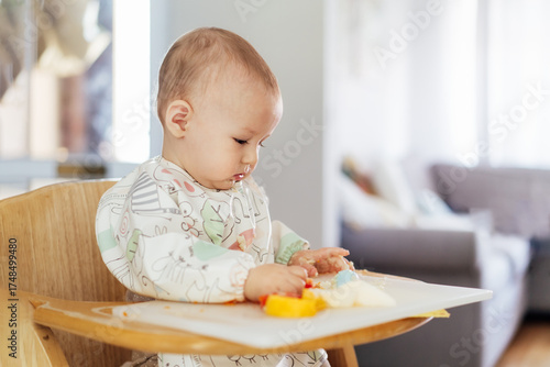 Billede på lærred Concentrated cute baby eating himself on high chair baby led weaning or blw