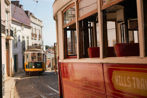 Vintage trams on cobblestone street in Lisbon, with white façades and tiled roofs. Transport heritage, urban aesthetics, Portugal.