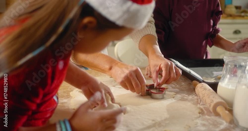 Grandmother and granddaughters pressing cookie cutters into dough and placing Christmas shapes on baking tray. A happy family prepares festive cookies together at home.