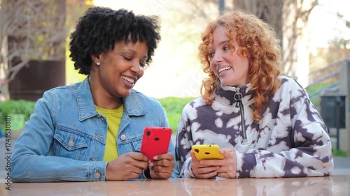 Two cheerful young women are enthusiastically using their smartphones, sharing a joyful experience as they engage with mobile applications, immersed in technology and connection with each other.