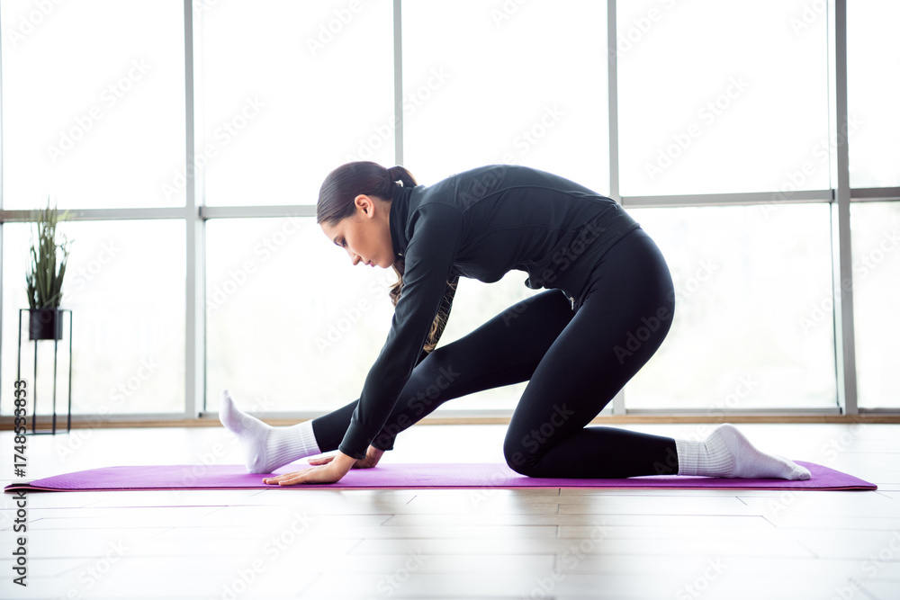 Fototapeta premium Charming woman performing a stretching exercise on a yoga mat in a bright airy room, engaging in a fitness routine