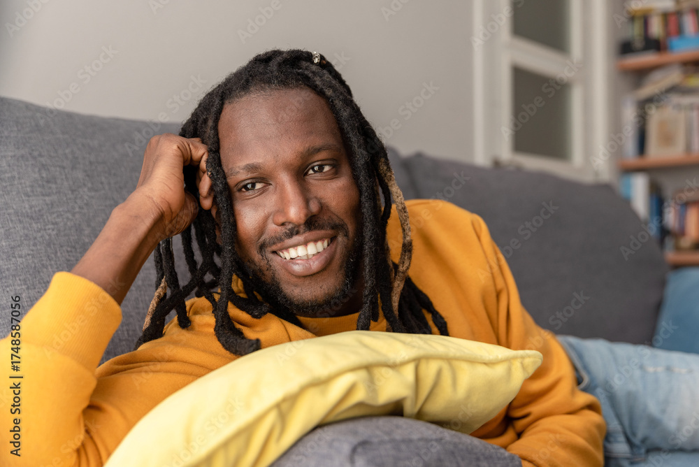 Fototapeta premium Young African american man with dreadlocks smiling while lying on a comfortable sofa at home