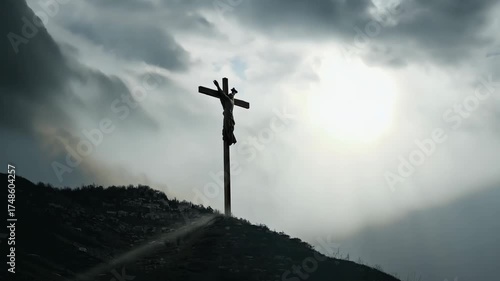A crucifix on a mountain during approaching storm. Dark clouds swirl, focused beam sunlight breaks spotlighting crucifix. A wind tattered cloth cross. Emotional, lighting powerful cinematic mood