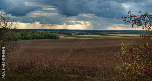 Arable field under a dramatic sky with rays of sunshine through the clouds at...
