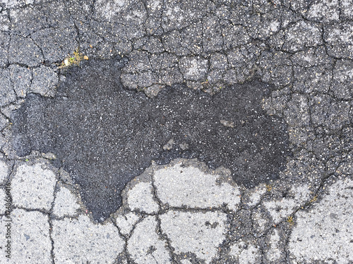 Cracked and damaged asphalt road surface with damp patch and distressed texture