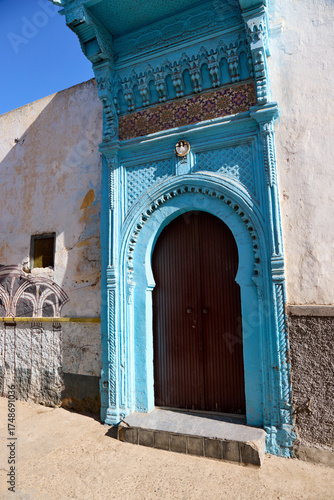 A striking blue door stands out on a sunny day in Al-Jadida, Morocco. The door is framed by aged walls, showcasing the blend of history and color in this charming location
