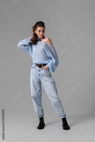 Young woman posing in light blue oversized sweater and baggy jeans against gray background