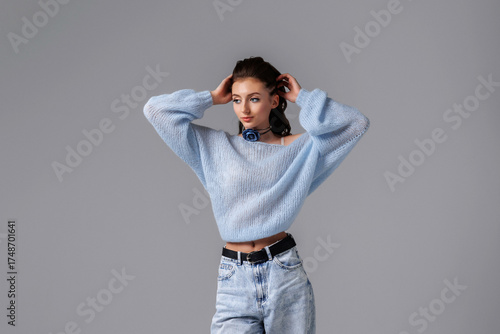 Young woman in blue sweater poses confidently against a gray background, highlighting fashion and style