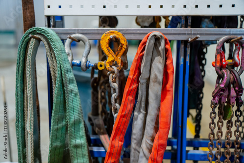 Fototapeta Industrial lifting straps, chains, and hooks organized on rack in mechanical wor