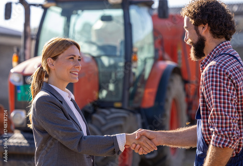 Farmer and businesswoman shaking hands in front of tractor