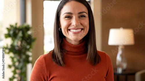 Smiling woman indoors holds a houseshaped key and keys toward the camera, suggesting new homeownership and warmth; soft lamp and blurred plants create cozy, welcoming living-room ambiance. sun-kissed