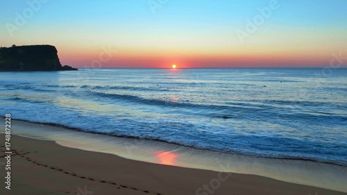 Soft waves roll ashore beneath a blush-toned sky, as the sun rises at Avalon Beach on Sydney’s Northern Beaches.