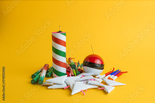  Composition of a variety of festive pyrotechnics, including rockets, a sphere, and triangular firecrackers, on a vibrant yellow background.