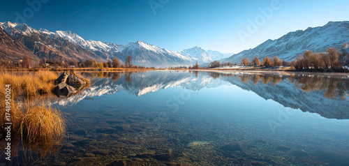 Serene mountain lake reflects autumn trees and snow capped peaks under clear blue sky