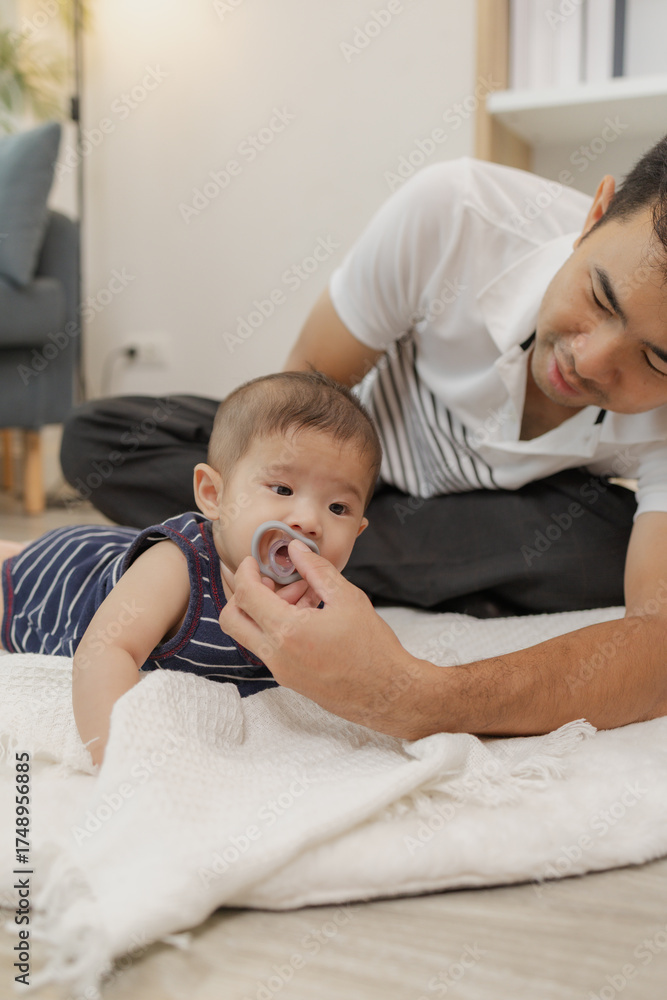 Obraz premium A father spends quality time with his baby, playing and bonding through gentle care and fun moments on a soft mat. The baby explores tummy time and pacifier use with support.